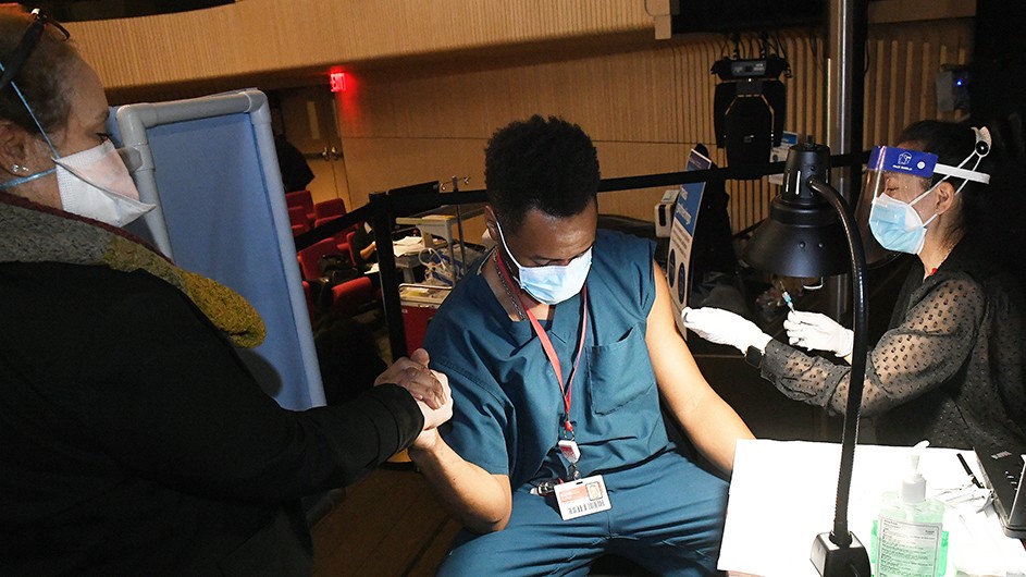 A man in scrubs and mask receives the vaccine. 