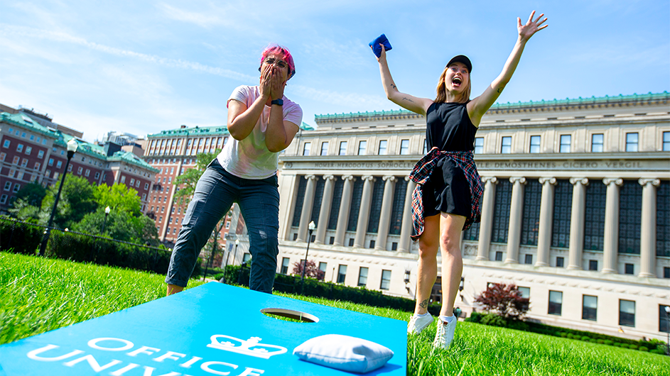 Students stand over a corn hole game. 