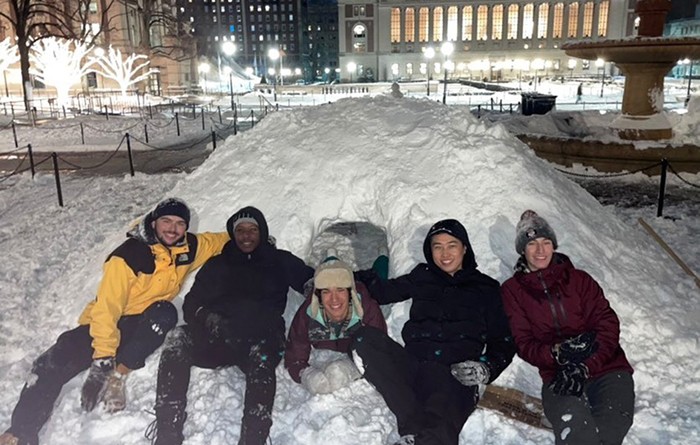 Students sit on a constructed snow igloo in front of Butler Library.