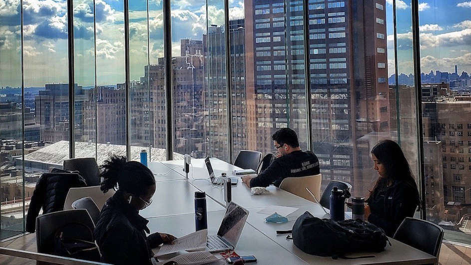 Three students studying at desk in a room with floor to ceiling glass windows