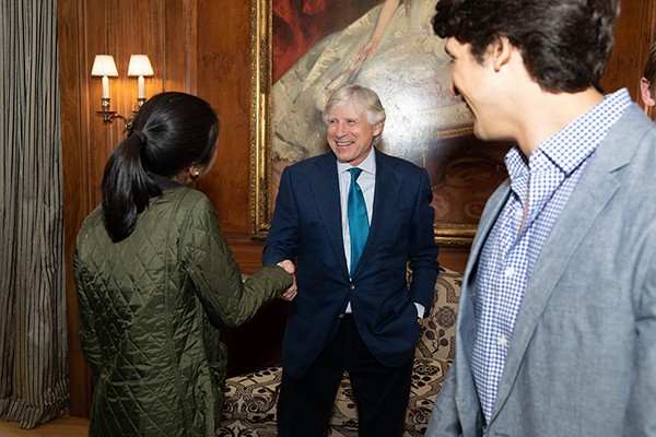 President Bollinger, a man in a suit, greets two students at an event. 