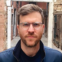 A man with short hair, a beard, and glasses, standing outside