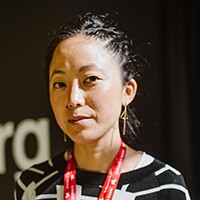 A woman with dark pulled-back hair in a black and white top. 