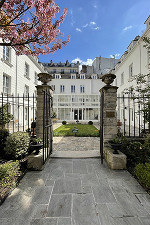 A sunlit courtyard in Paris, surrounded by white buildings and a stone gate. 