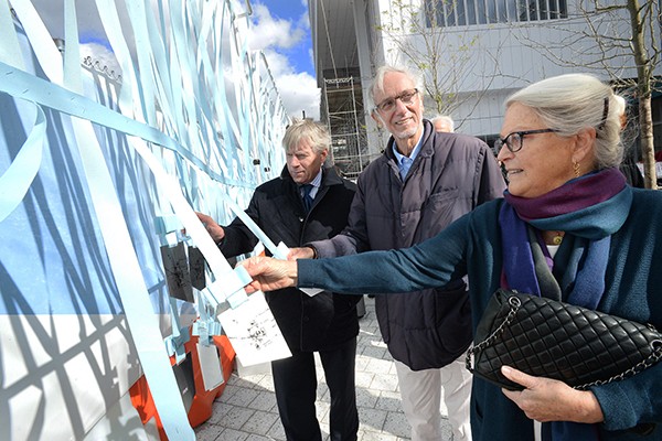 Lee Bollinger, Renzo Piano, and Jean Magnano Bollinger stand outside examining metal replicas of the Manhattanville Master Plan on strings. 