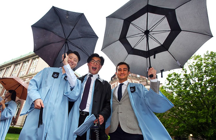 A little drizzle couldn't dampen the spirit of these alumni who returned to campus to finally celebrate their degrees in person. Photo by Bruce Gilbert. Three Columbia students with umbrellas line up for the Academic Procession.