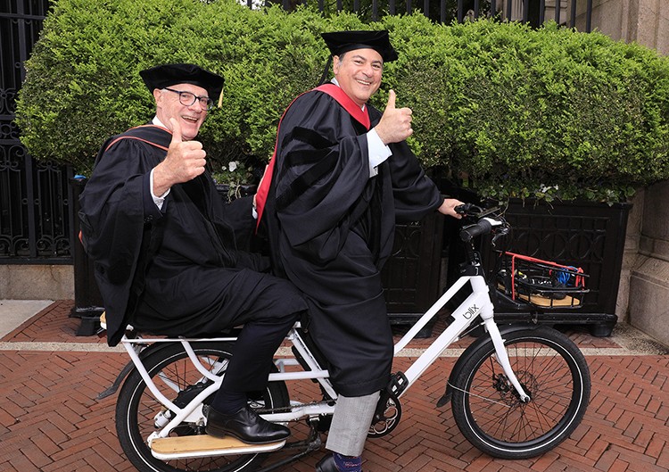 Climate School Deans Alex Halliday and Jason Bordoff enter the Climate School ceremony on a bike. 