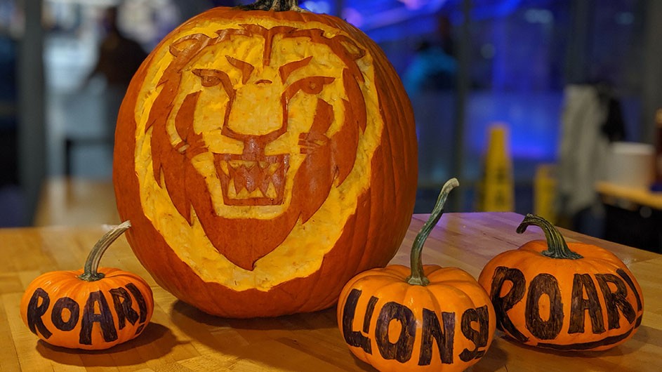 A pumpkin carved with a lion's face and three small pumpkins reading "Roar Lion Roar!"