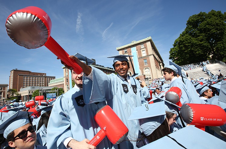SEAS students in cap and gowns wave inflatable red hammers at Commencement. 
