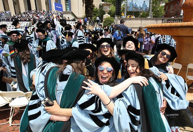 Graduates hug in celebration after their Columbia degrees are conferred. Photo by Bruce Gilbert. Students in caps and gowns hug in celebration after degrees are conferred.