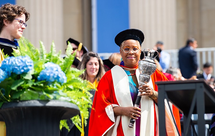 Mabel O. Wilson, Nancy and George Rupp Professor of Architecture, Planning and Preservation and Director of the Institute for Research in African American Studies, was the Mace Bearer for Columbia at University Commencement 2022. The mace symbolizes the university president’s ability to confer degrees on graduates. Photo by Diane Bondareff. Mabel Wilson holds to the ceremonial mace in a red gown and black hat.