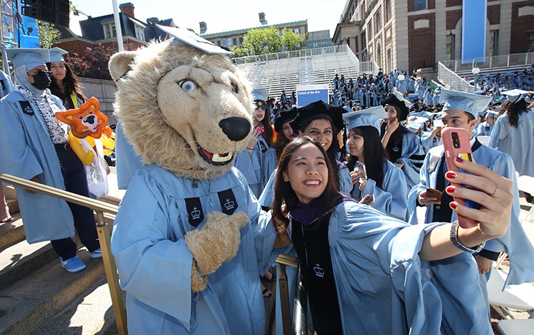 Columbia's mascot Roar-EE poses with a student during the academic procession. Photo by Bruce Gilbert. Roar-EE poses with a student during the academic procession