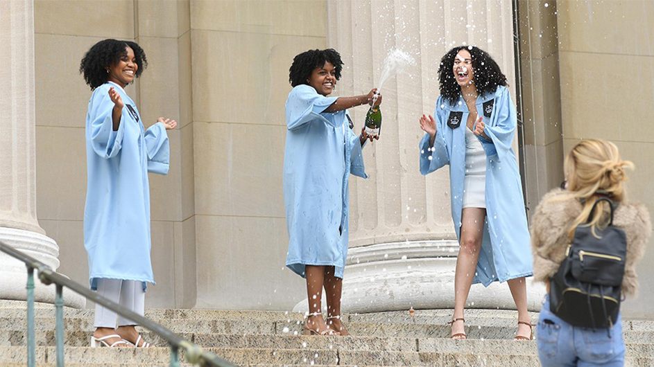 Three women in Columbia regalia pop champagne on Low Steps. 