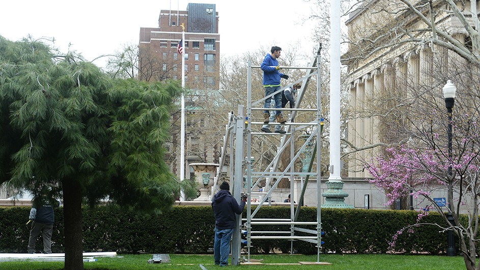 Two workers set up the bleachers on Low Plaza. 