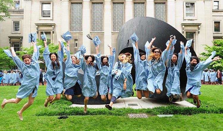 Graduates jump in front of the Curl statue in front of Uris Hall.