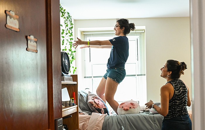 A student jumps on their dorm bed to show off an element of the wall decor. 