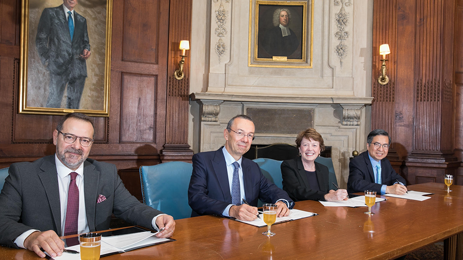 four people sit at a table signing documents