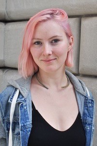 Ellie Houghtaling, 2022 graduate of Columbia Journalism School. She has pink hair and is wearing a jean jacket and a black shirt