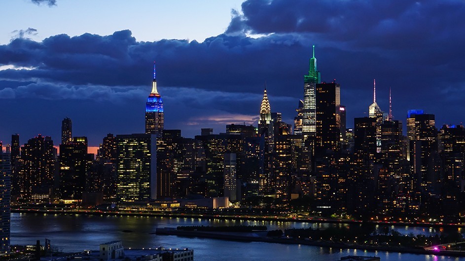 The Empire State Building glows blue and white against Manhattan skyline