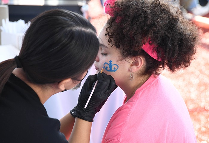 Pre- and post-game activities included face painting and corn hole. Photo by Eileen Barroso/Columbia College. A girl in a pink shirt gets a Columbia crown painted on her face.