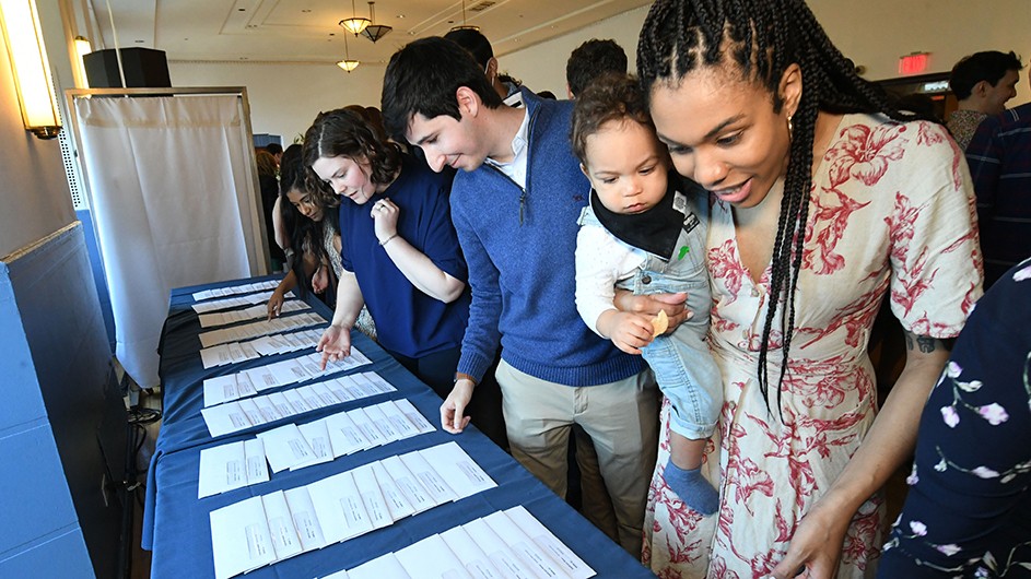A student with a baby looks down at the Match day envelopes. 