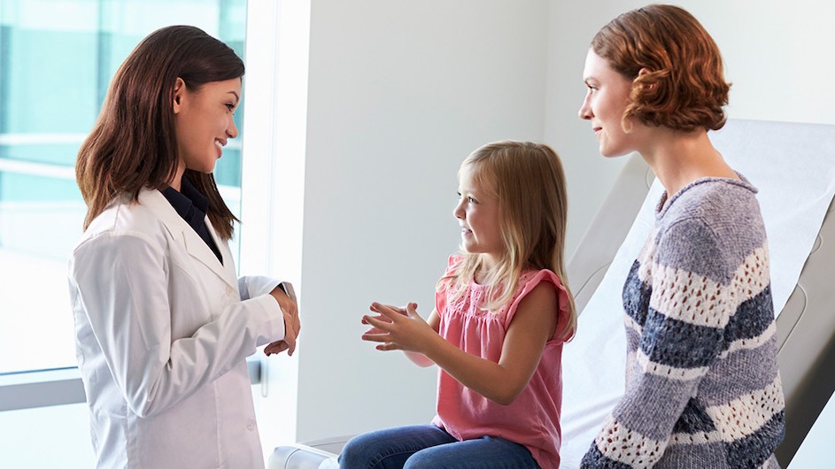 A photo of a woman talking to a girl and her mother in a doctor's office