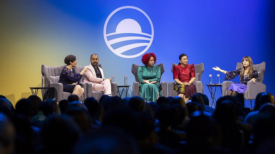 Five people sitting in chairs on a stage, having a discussion. 