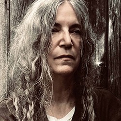 Patti Smith, a woman with long, grey hair in a white t-shirt and black top. 