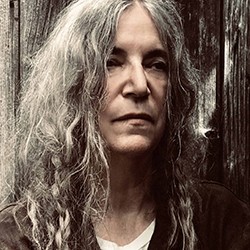 Patti Smith. Photo: Steven Sebring. Patti Smith, a woman with long, grey hair in a white t-shirt and black top.