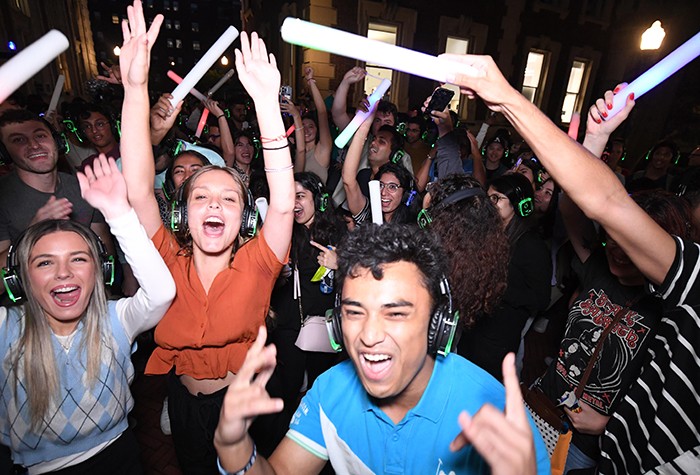 A scene from Low-Lapalooza, a silent disco hosted by the Office of University Life on Columbia's campus to welcome students to campus. Welcome Home Columbia activities continued through September 16 and included a scavenger hunt, Columbia Quest. Photo by Eileen Barroso. Students wear headphones and shake glow sticks on Columbia's campus.