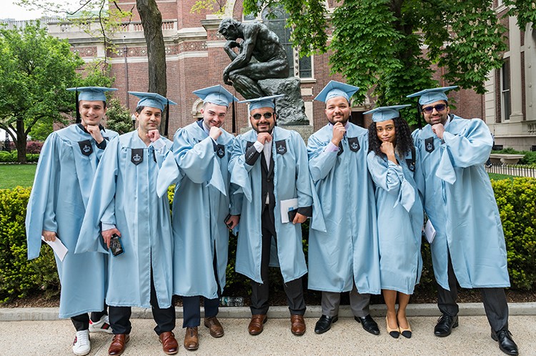 School of Professional Studies students pose in front of the thinker statue in caps and gowns. 
