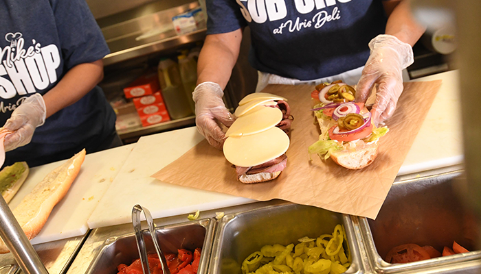 A view of sandwich ingredients being places on a sub. 