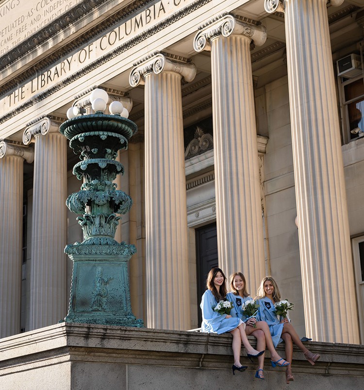 Three students in regalia hold flowers near Low Library