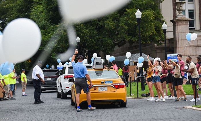 The end of move-in also means a series of goodbyes and cheers as a line of cars exits College Walk. Photo by Diane Bondareff. A taxi drives away amid a College WAlk lined with balloons.
