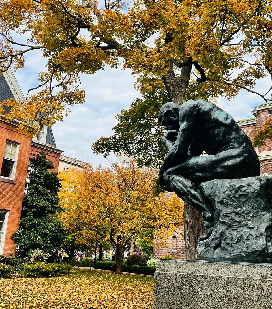 Vibrant yellow and orange leaves overhang from trees above the statue of "The Thinker" on Columbia's Morningside campus.