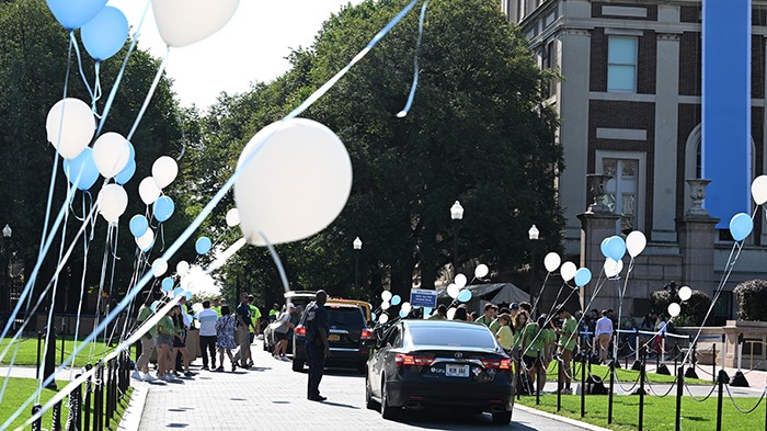Cars pull up on College Walk to unload move-in items for students. Balloon wave in the breeze.