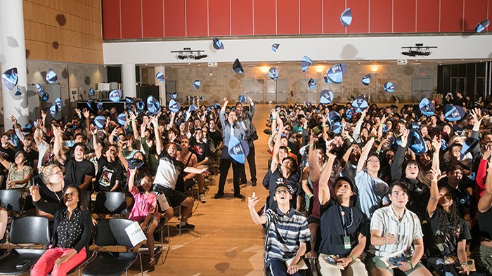 A whole group of students and Dean Shih-Fu Chang throw beanies in the air.
