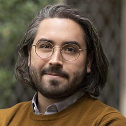 A man with dark, medium-length dark hair, glasses, a mustache and beard. 