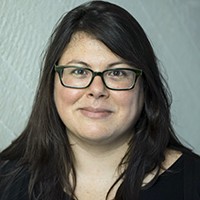 A woman with long dark hair and glasses, in a black top. 