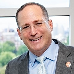 A man with short hair in a suit and tie, smiling.