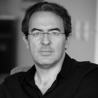 A man with short, dark hair and glasses, in a black shirt. 