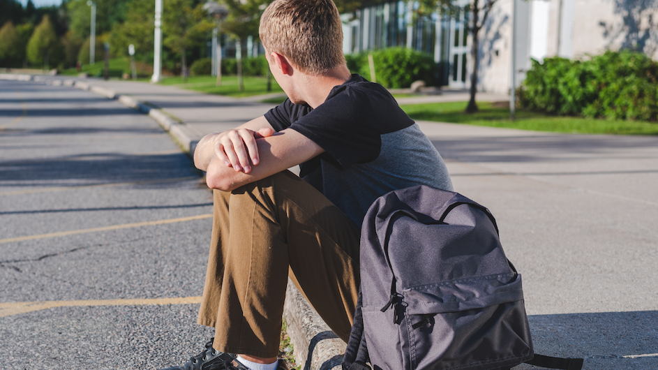 A teenager sitting on a sidewalk.