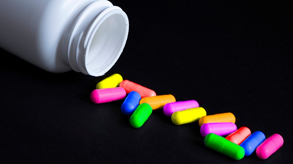 A pill bottle with colorful pills spilling from it.
