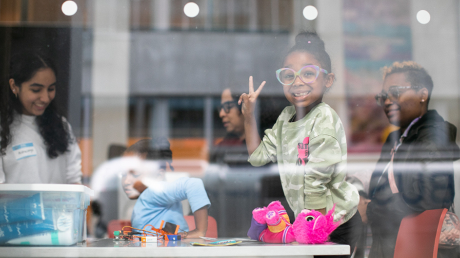 A little girl gives a peace sign during Saturday Science at Community Day. 