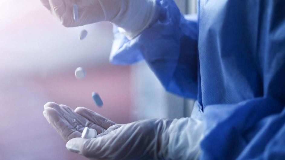 A gloved hand holding prescription pills.