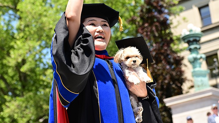 A faculty member holds a dog in regalia. 