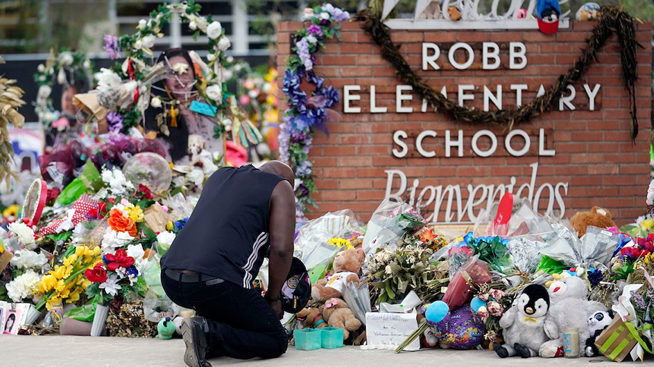 a man kneels before a memorial in front of a school