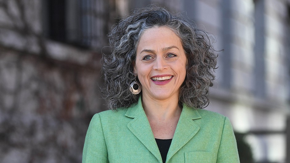 Columbia researcher Lisa Dale, wearing a light green blazer, smiles and stands on the sidewalk opposite Columbia Law School on 116 Street in New York City.