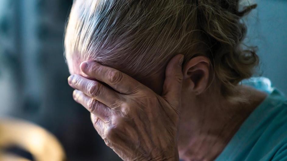 An older person holding their head in their hands.