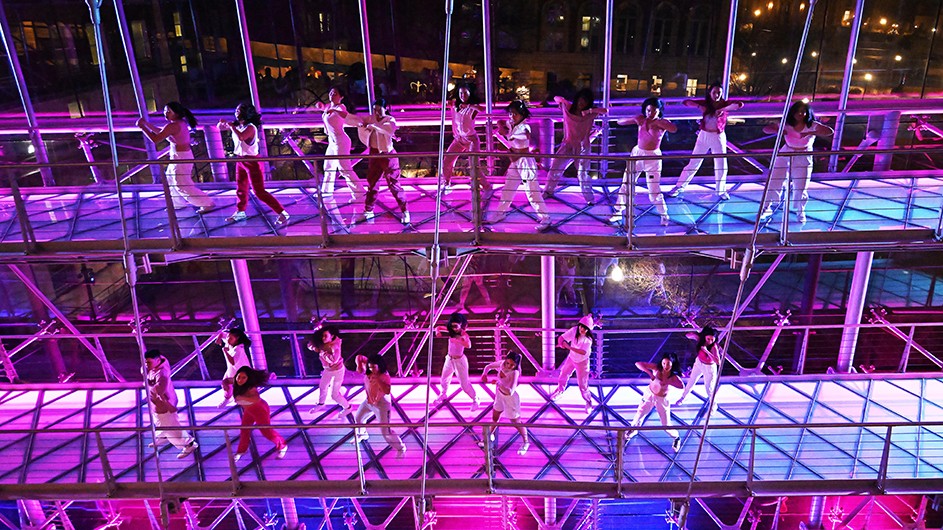 Twenty CU Generation hip-hop team members dance on illuminated purple, pink, and blue ramps at Lerner Hall for Glass House Rocks at Columbia University at night.